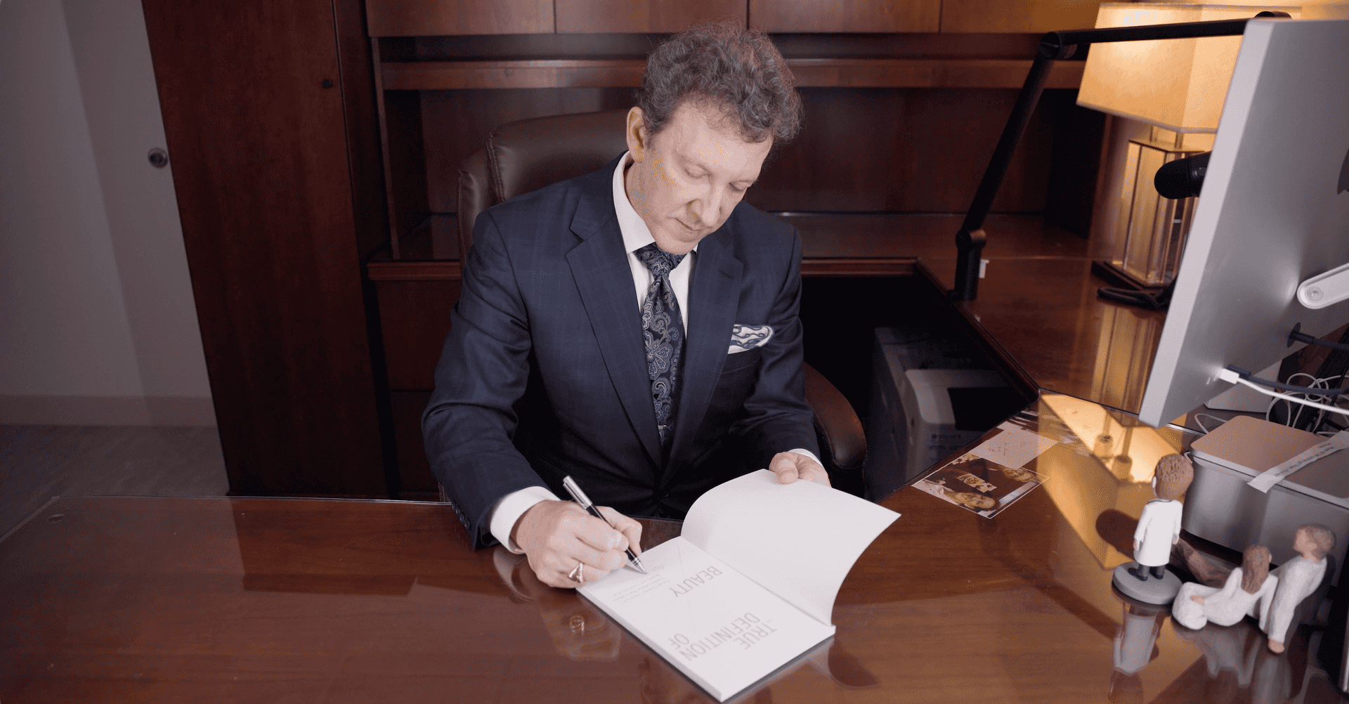 Adam Scheiner, M.D. signing a copy of his book at his office desk.