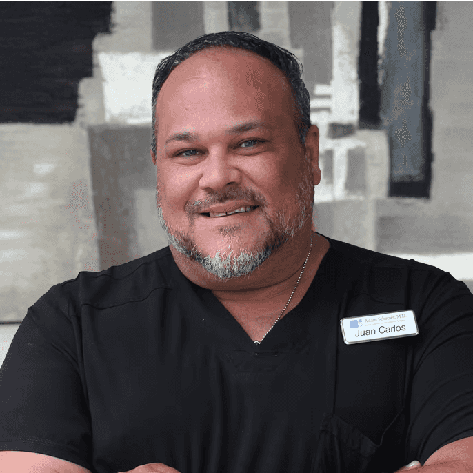 Juan crosses his arms in black scrubs with a subtle smile.