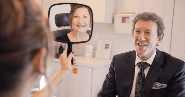 Dr. Adam Scheiner with a patient, sharing her reflection in a hand mirror after her procedure